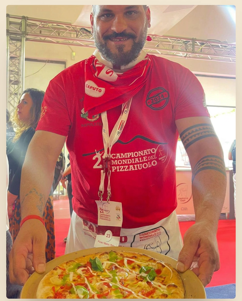 Nuni at the Campionato Mondiale del Pizzaiuolo, holding a freshly baked pizza.
